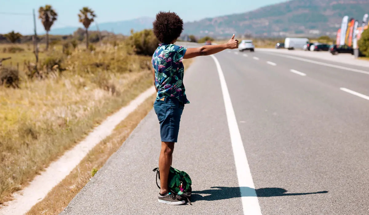 Homme faisant de l'auto-stop aux abords d'une route